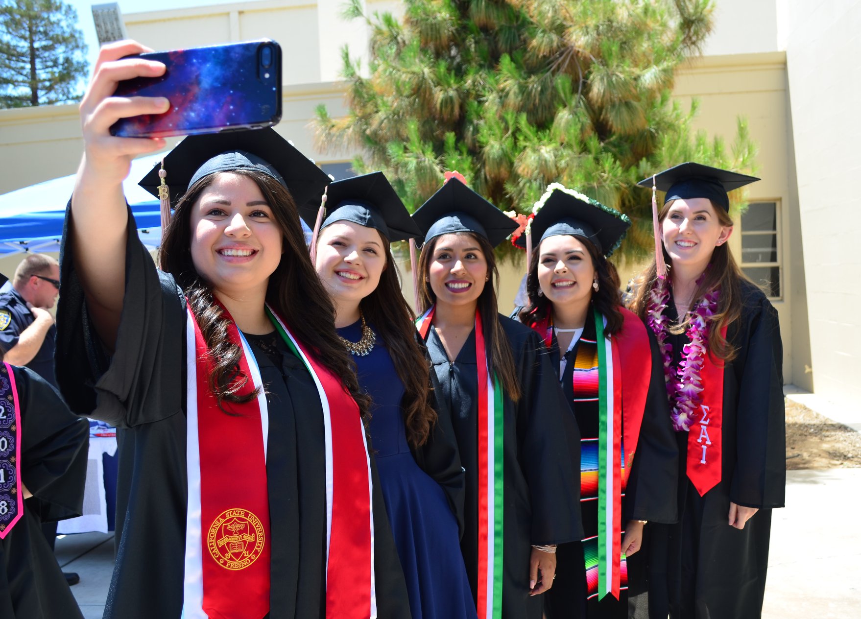 A group of students lined up in graduation regalia with the lead student taking a "selfie" of the group