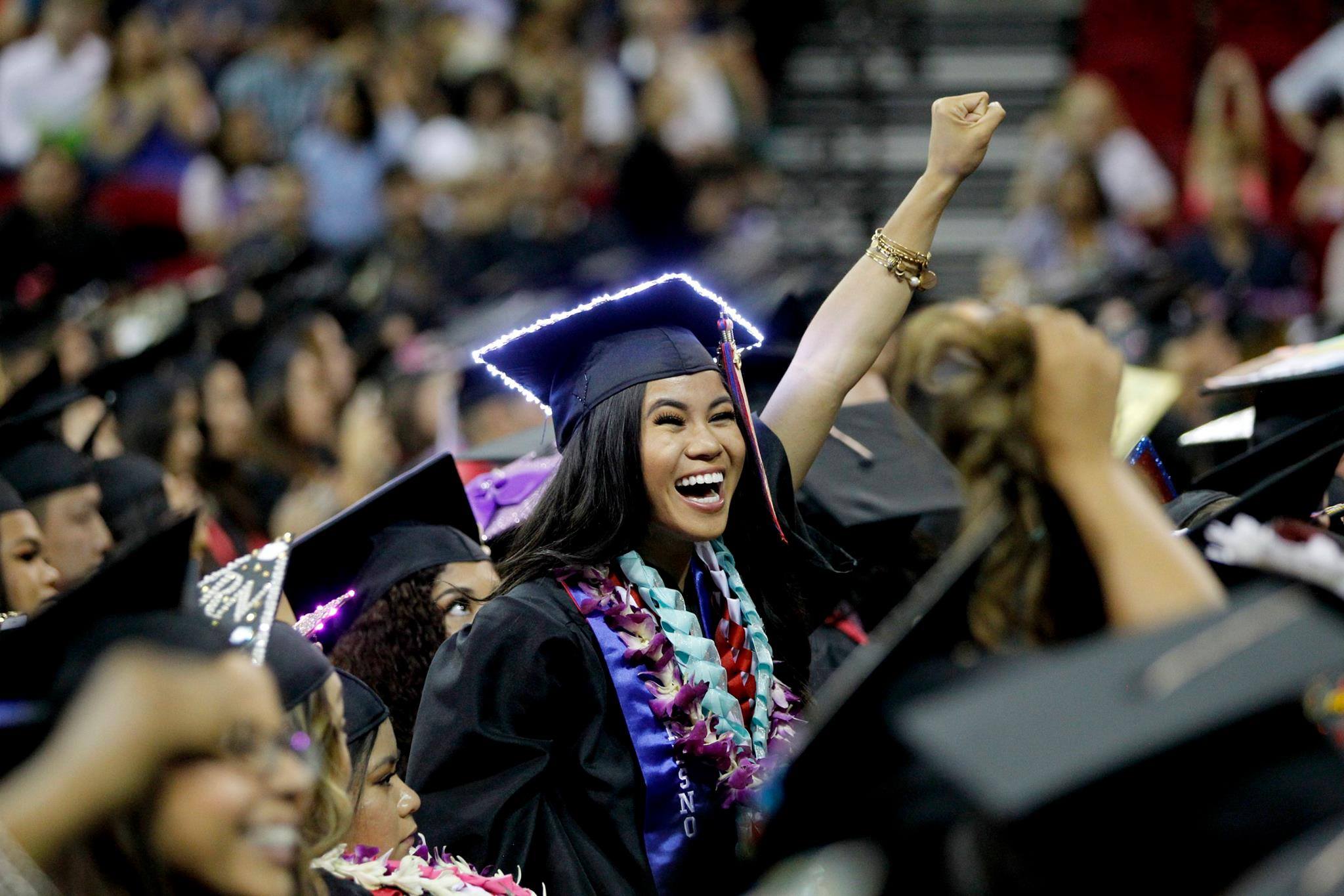 A student celebrating her graduation with her left fist raised in the air