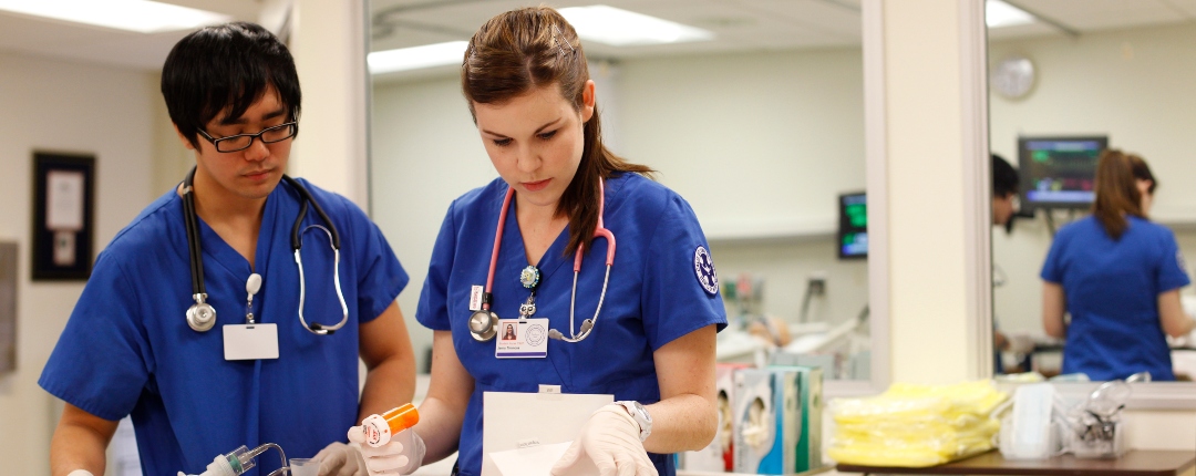 Two students in nursing scrubs view paperwork