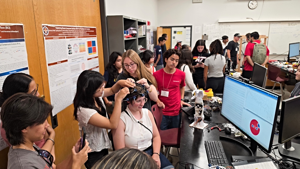 Students gather around a student wearing headset while viewing brainwave signals on screen 