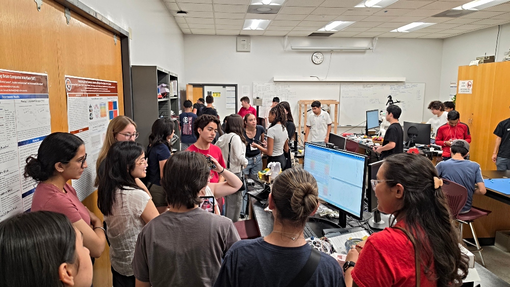 Students gather around a student wearing headset while viewing brainwave signals on screen 