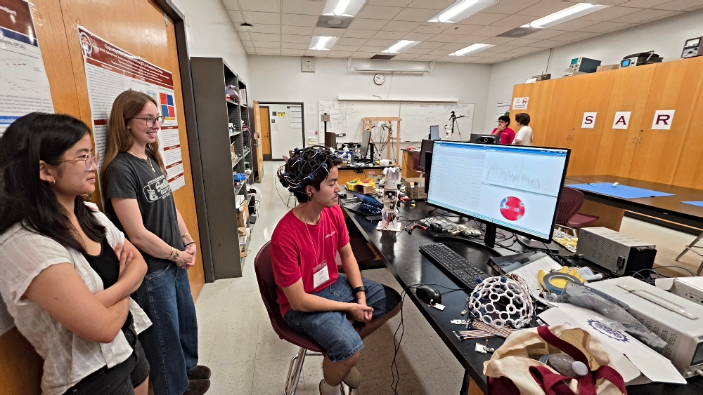 Students gather around a student wearing headset while viewing brainwave signals on screen 