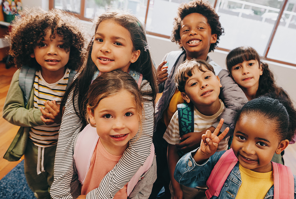 Seven school-aged children at school and posing for the camera in joy.