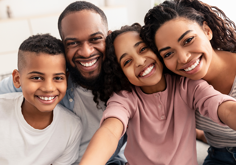 A family of four with two children, one father, and one mother smile for the camera.