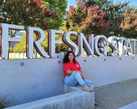 student sits in front of Fresno State sign